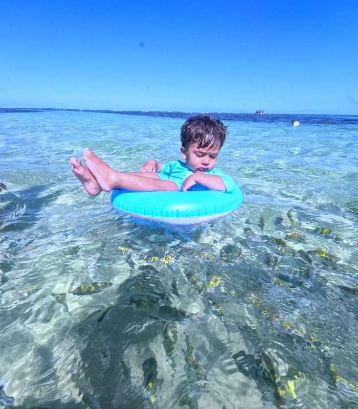 Criança flutuando com boia na água transparente das Piscinas Naturais do Seixas