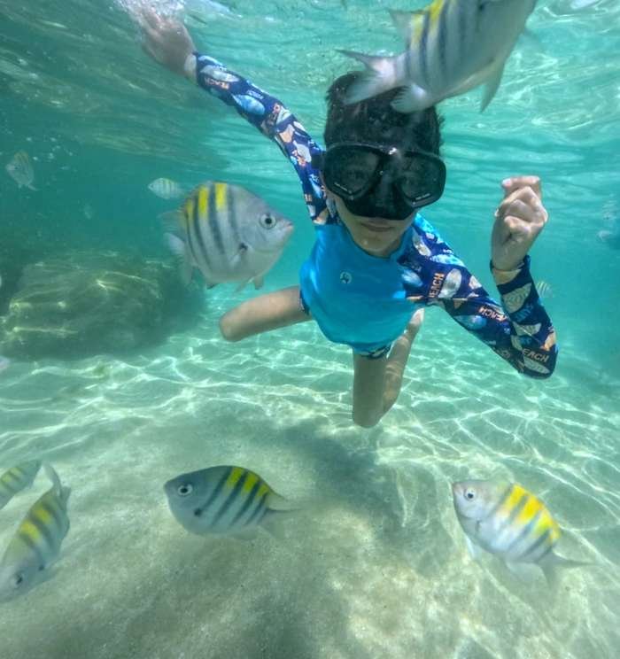 Criança fazendo snorkel nas Piscinas Naturais do Seixas cercada de peixes coloridos